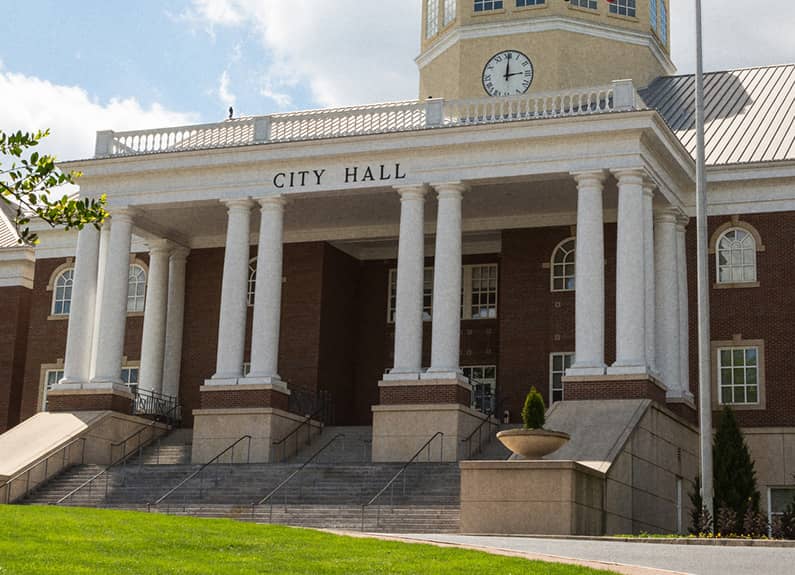 Brick city government building featuring clock tower, columns and staircase leading to the entrance